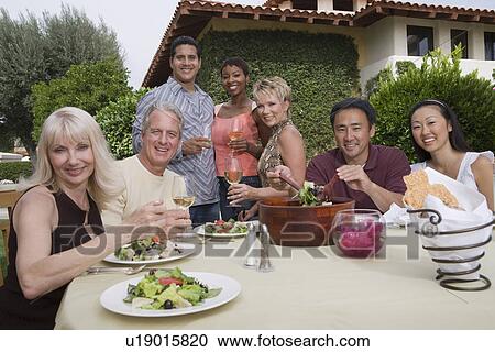 Stock Image - Group of friends dining outdoors, portrait. Fotosearch
