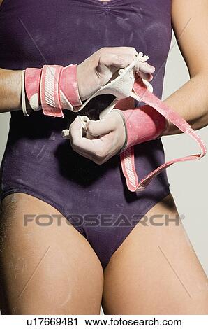 Stock Image - Gymnast (13-15) putting on palm guards, mid section. Fotosearch