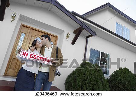 Stock Photo - Homeowners standing in front of house, portrait. Fotosearch