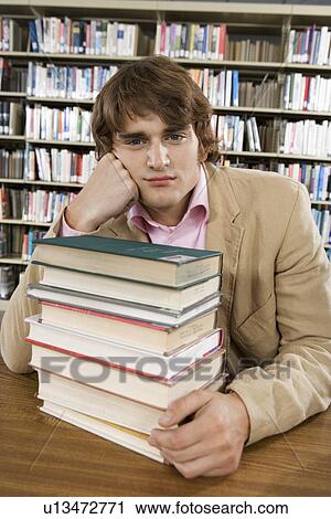 Stock Image - Male college student in library with stack of books. Fotosearch