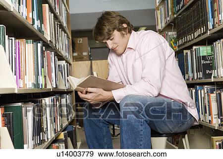 Stock Photo - Male college student sitting, reading in library. Fotosearch
