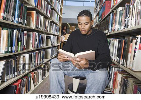 Stock Photo - Male student sitting, reading in library. Fotosearch