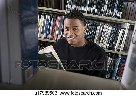 Stock Image - Male University student reading in library, portrait. Fotosearch
