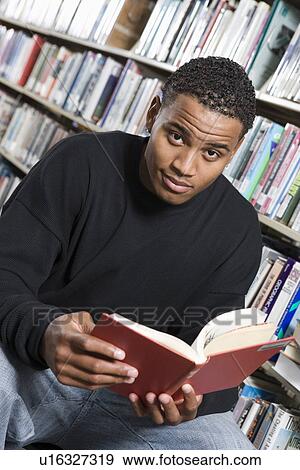 Stock Photo - Male University student reading in library, portrait. Fotosearch