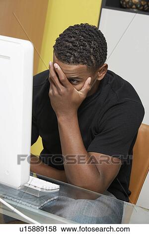 Man covering face with hand sitting at computer View Large Photo Image Stock Photo - Man covering face with hand sitting at computer. Fotosearch