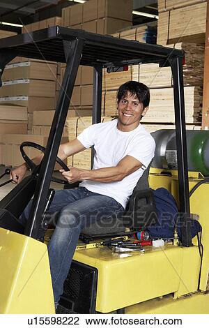 Stock Image - Man driving forklift in warehouse full of wood. Fotosearch