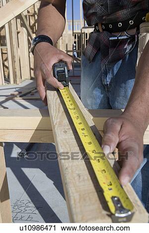 Stock Image - Man measuring half constructed wall with tape measure. Fotosearch