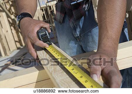 Stock Image - Man measuring half constructed wall with tape measure. Fotosearch