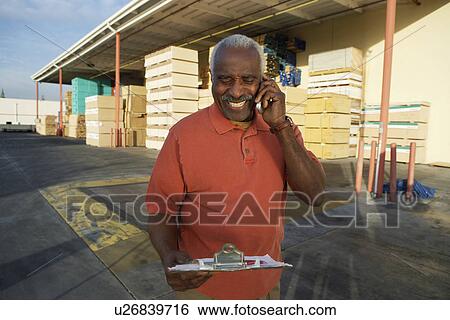 Stock Photograph - Man on cell phone by warehouse of wood. Fotosearch