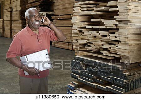 Stock Image - Man on cell phone in warehouse of wood. Fotosearch