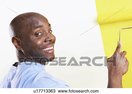 Stock Image - Man painting interior wall yellow, portrait. Fotosearch