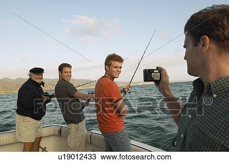 Stock Image - Man photographing family fishing on boat. Fotosearch