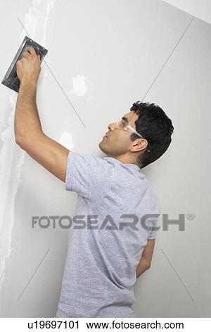 Stock Image - Man sanding interior wall. Fotosearch