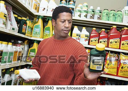 Stock Image - Man selecting plant care products in shop. Fotosearch