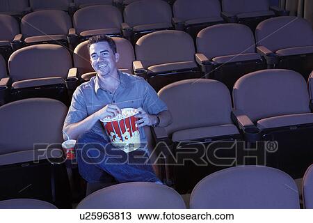 Stock Image - Man sitting alone in empty theatre eating popcorn, Watching Movie. Fotosearch