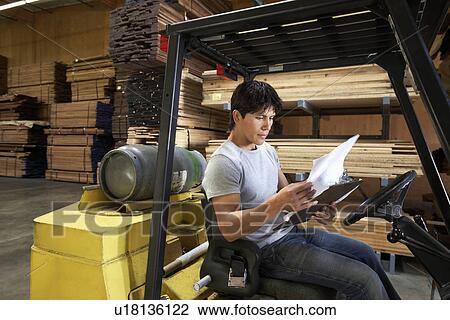 Man sitting in forklift reading paperwork in warehouse View Large Photo Image Stock Image - Man sitting in forklift reading paperwork in warehouse. Fotosearch