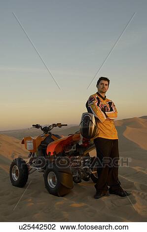 Man standing by quad bike in desert at sunset View Large Photo Image Stock Image - Man standing by quad bike in desert at sunset. Fotosearch