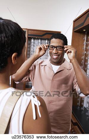 Stock Image - Man trying on glasses at opticians. Fotosearch