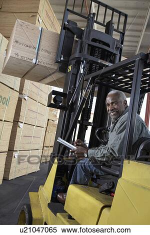Stock Photography - Man using forklift to lift box in warehouse. Fotosearch