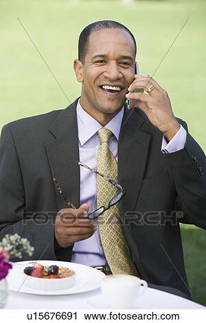 Stock Image - Man using mobile phone at outdoor table. Fotosearch