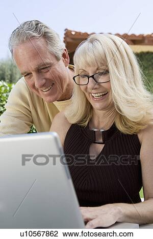 Stock Image - Mature couple using laptop in back yard. Fotosearch