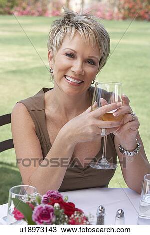 Stock Image - Mature elegant woman sitting at outdoors, holding wine glass. Fotosearch