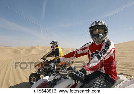 Stock Image - Men riding quad bikes over desert. Fotosearch