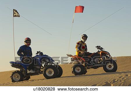 Stock Photo - Men sitting on quad bikes in desert. Fotosearch