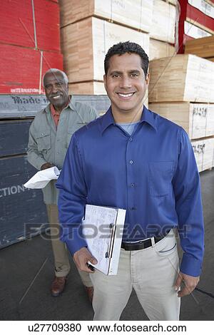 Stock Image - Men with clipboards in front of stacks of wood. Fotosearch