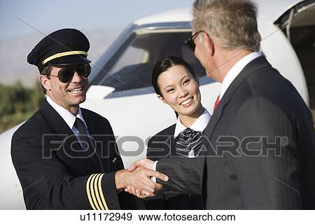 Stock Photo - Mid-adult airline pilot and senior businessman shaking hands.. Fotosearch
