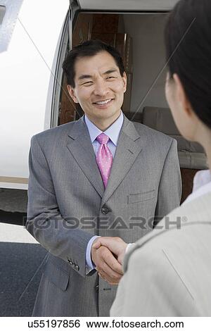 Stock Photograph - Mid-adult Asian businessman shaking hands with mid-adult businesswoman in front of private plane.. Fotosearch