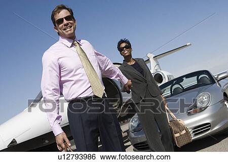 Mid-adult business couple outside of car and airplane. View Large Photo Image Stock Photograph - Mid-adult business couple outside of car and airplane.. Fotosearch