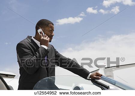 Mid-adult businessman standing in convertible and using mobile phone. View Large Photo Image Stock Image - Mid-adult businessman standing in convertible and using mobile phone.. Fotosearch
