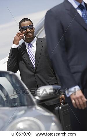 Stock Image - Mid-adult businessman using mobile phone outside of car.. Fotosearch