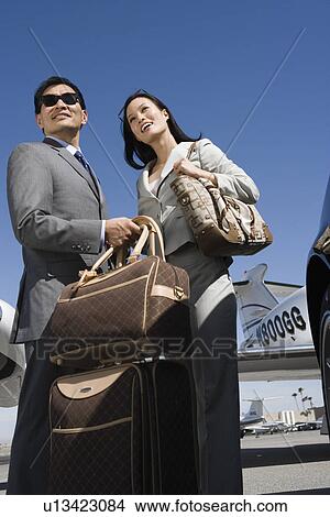 Picture - Mid-adult businesswoman and businessman standing in front of car with their luggage.. Fotosearch