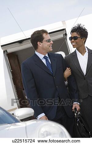Picture - Mid-adult businesswoman and businessman in front of airplane.. Fotosearch