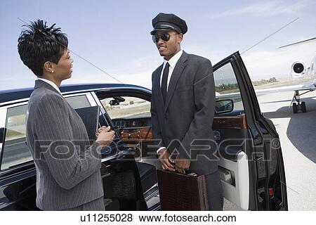 Stock Photo - Mid-adult businesswoman and mid-adult chauffeur standing in front of limousine and talking.. Fotosearch