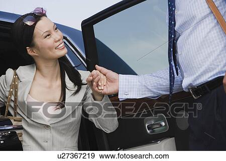 Stock Photo - Mid-adult businesswoman getting of car, man assisting.. Fotosearch