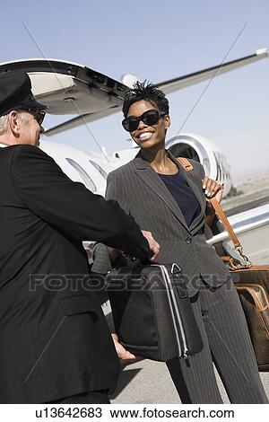 Stock Image - Mid-adult businesswoman giving suitcase to chauffeur in front of airplane. Fotosearch