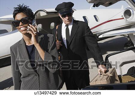 Stock Photo - Mid-adult businesswoman talking on phone while chauffeur is waiting. Fotosearch