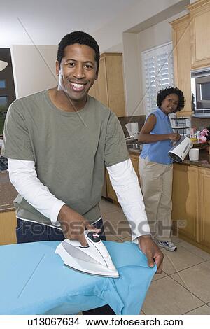 Mid-adult couple at domestic kitchen, man ironing View Large Photo Image Picture - Mid-adult couple at domestic kitchen, man ironing. Fotosearch