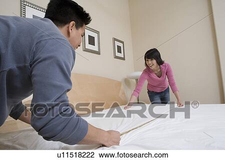 Stock Image - Mid-adult couple making a bed. Fotosearch