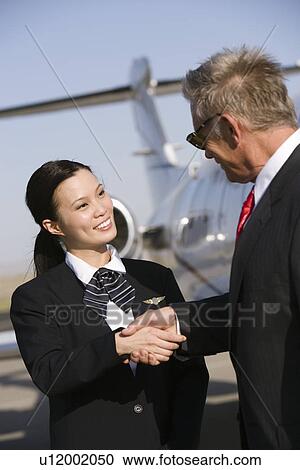 Stock Image - Mid-adult flight attendant and senior businessman shaking hands.. Fotosearch