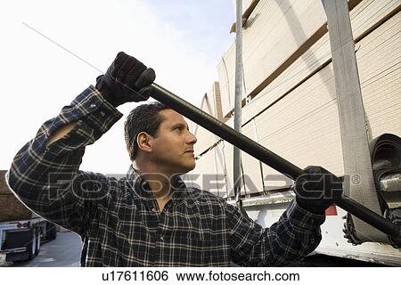 Mid-adult man adjusting strapping of truck loaded with wood View Large Photo Image Stock Photograph - Mid-adult man adjusting strapping of truck loaded with wood. Fotosearch