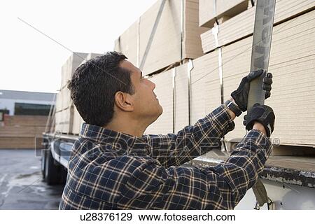 Stock Photo - Mid-adult man checking strapping of truck loaded with wood. Fotosearch