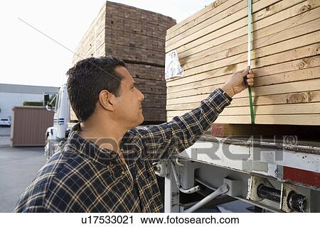Stock Image - Mid-adult man checking truck loaded with wood. Fotosearch