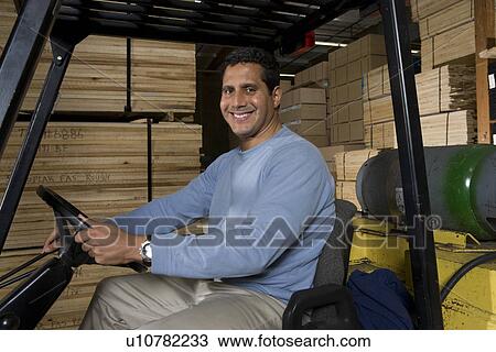 Stock Image - Mid-adult man driving forklift at warehouse. Fotosearch