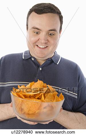 Stock Image - Mid-adult man holding glass bowl of potato chips. Fotosearch