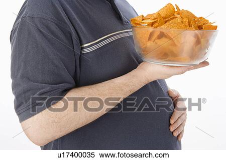 Stock Photography - Mid-adult man holding glass bowl of potato chips, mid section. Fotosearch