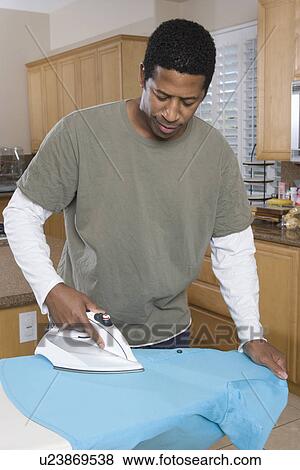 Stock Photo - Mid-adult man ironing shirt in domestic kitchen. Fotosearch